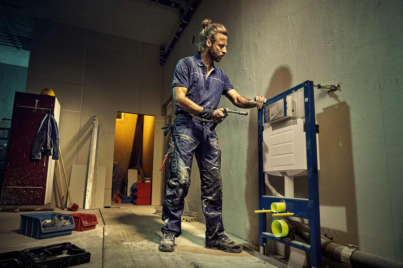 Ein Installateur montiert einen Spülkasten in einem Rohbau.