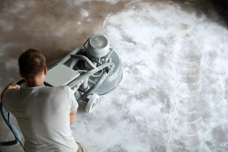 Mann schleift Betonboden mit Bodenschleifmaschine