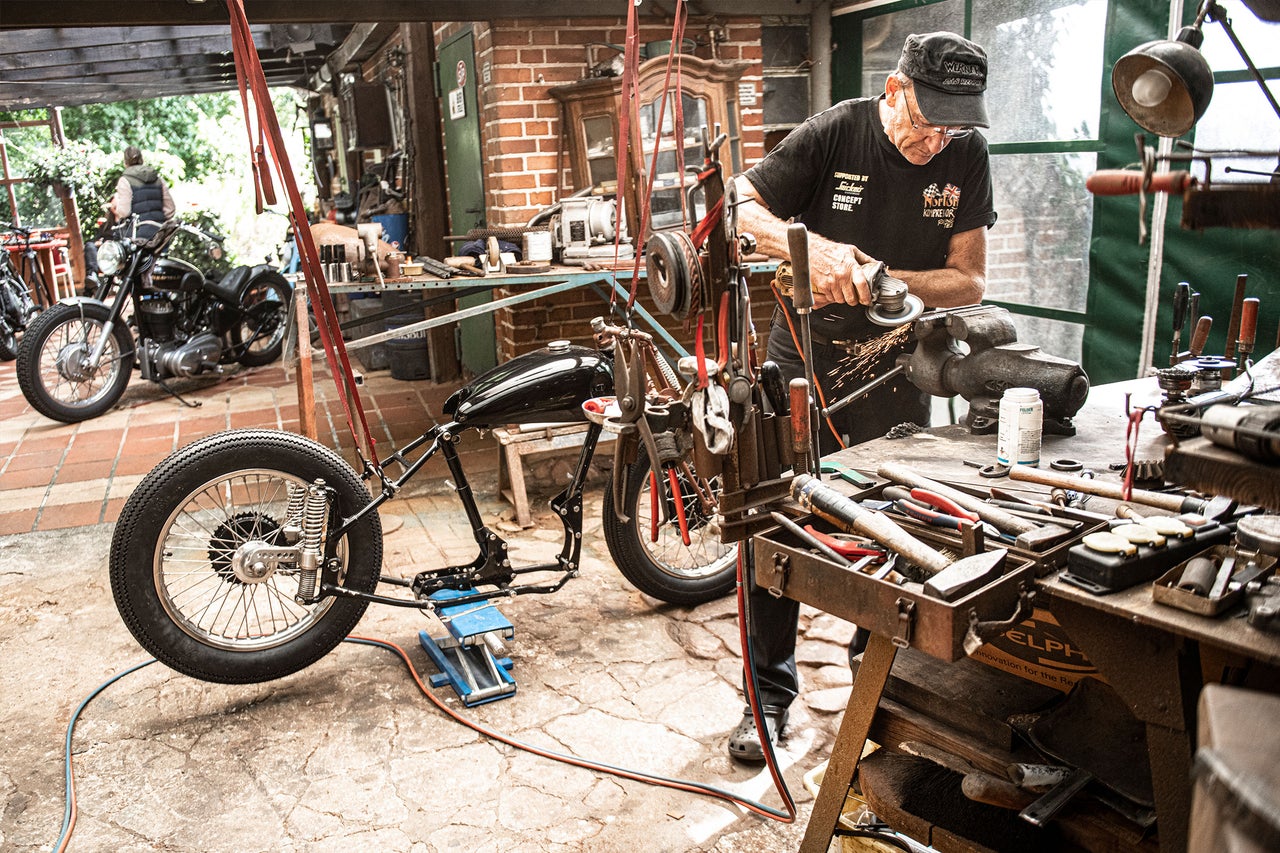Werkstatt mit Motorrad, Werkbank und Handwerker bei der Arbeit.