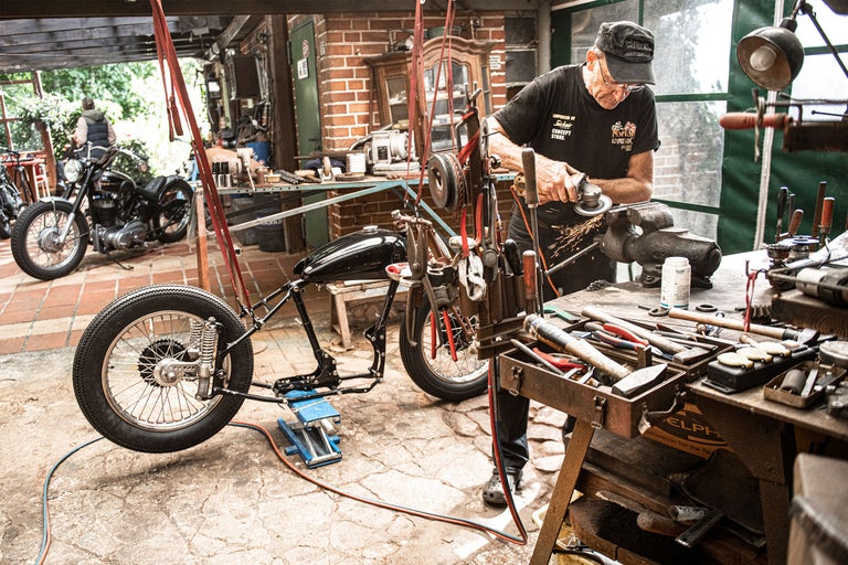 Werkstatt mit Motorrad, Werkbank und Handwerker bei der Arbeit.