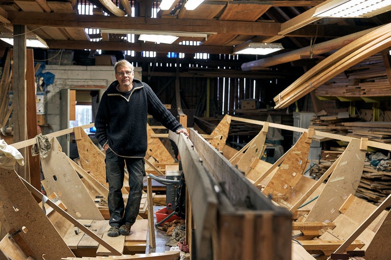 Mann steht in einer Werkstatt vor einem Holzboot im Bau
