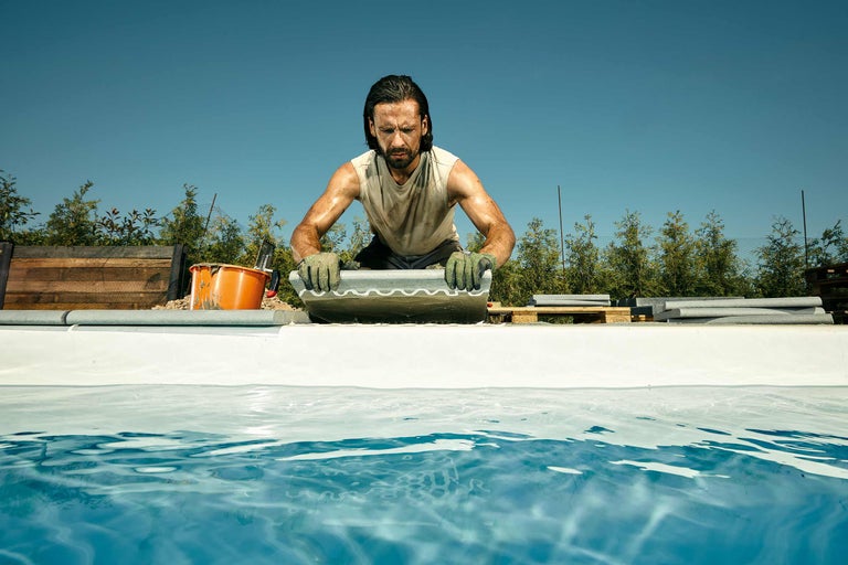 Ein Mann verlegt Poolrandsteine an einem Pool