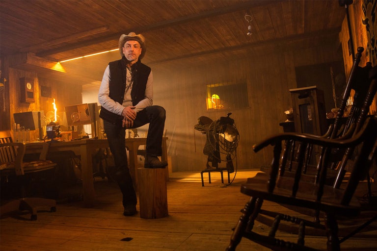 Mann mit Cowboyhut in einem rustikalen Raum mit Holzmöbeln und Beleuchtung