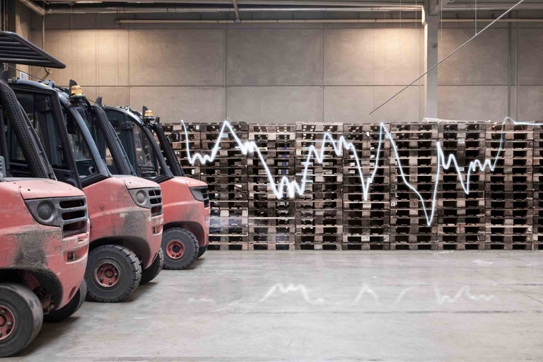 Reihe von Gabelstaplern vor einem Stapel Paletten mit einem Diagramm, das Wertschwankungen darstellt