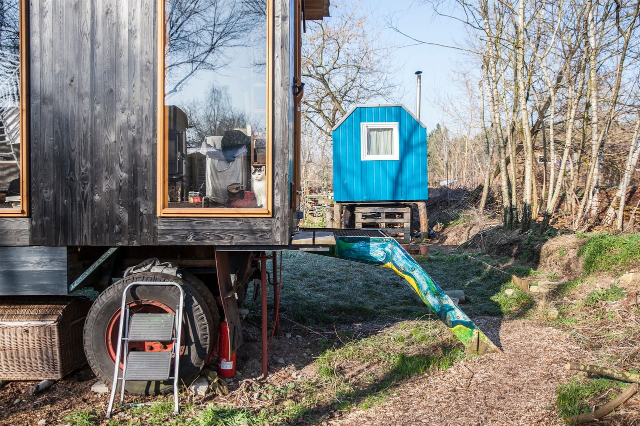 Szene mit einem Wohnwagen mit Holzverkleidung und einem kleinen Haus im Hintergrund.