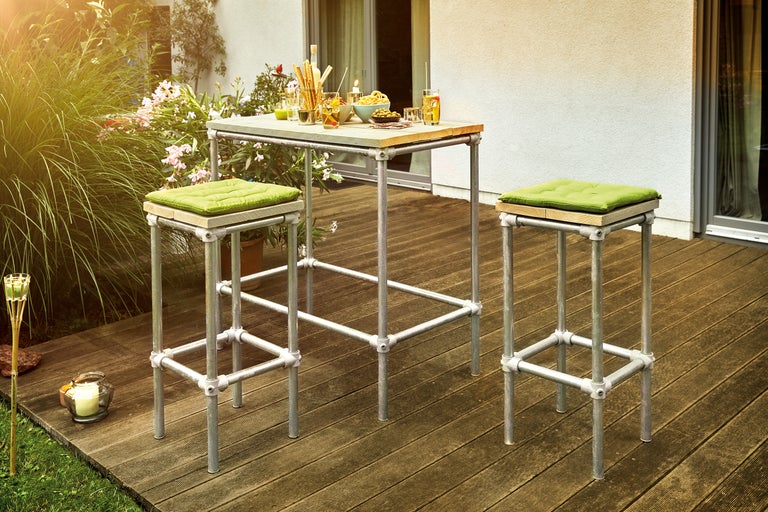 Gartenszene mit Stehtisch und zwei Barhockern aus Metallrohr und Holzelementen
