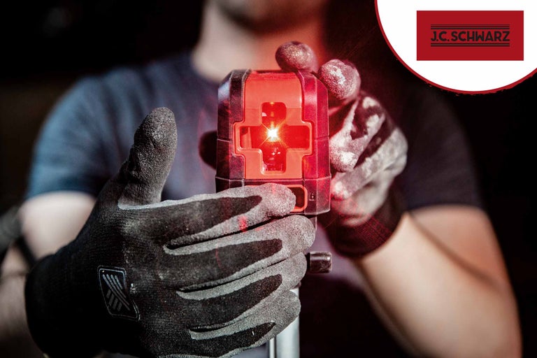 Eine Person hält einen Kreuzlinienlaser mit Handschuhen in der Hand. J.C. Schwarz Logo.