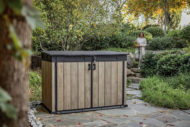 Gartenschrank aus Holz und Metall im Garten mit einer Frau im Hintergrund