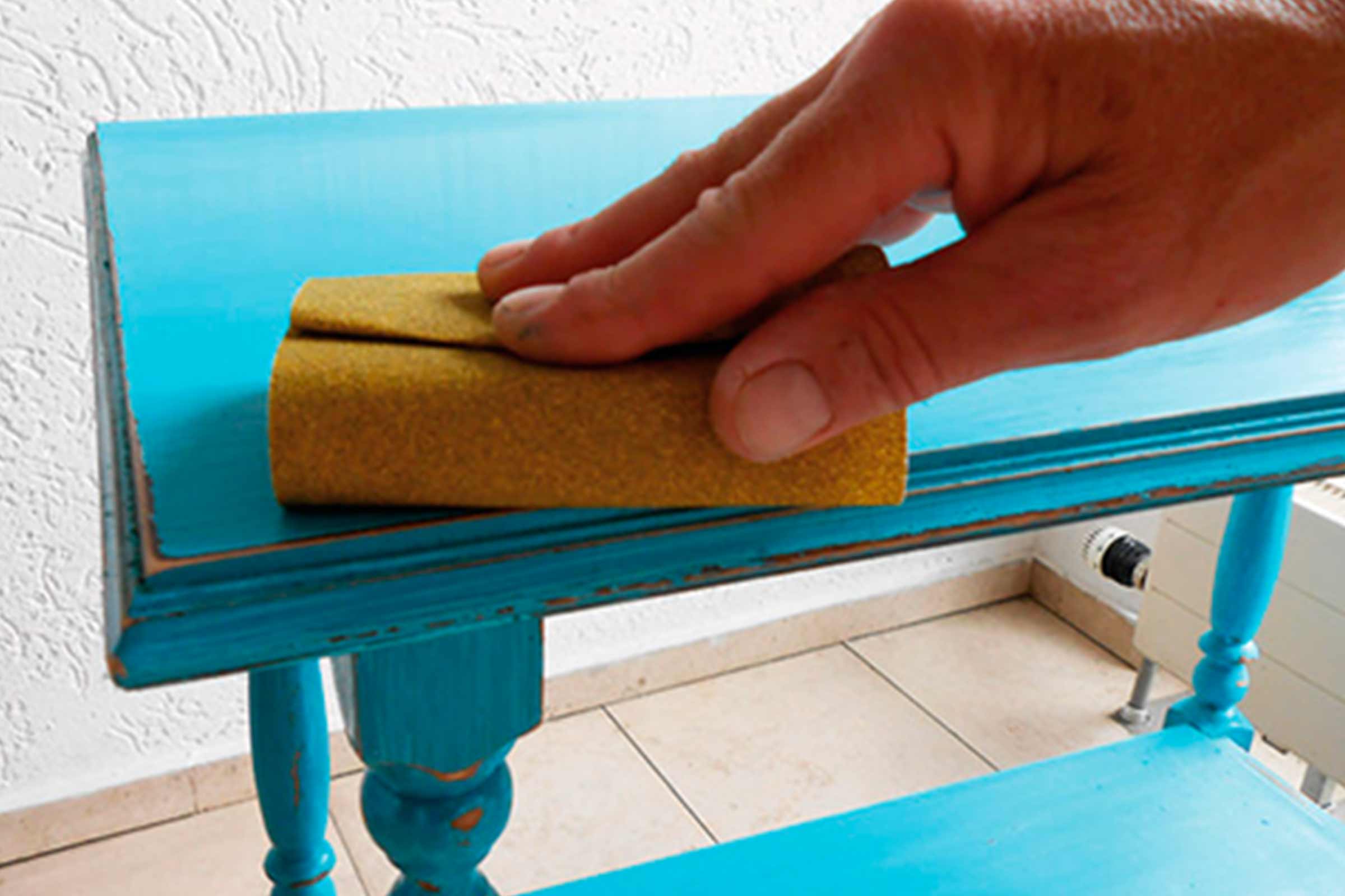 Eine Person schleift einen Tisch mit Schleifpapier.