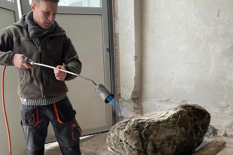 Ein Mann erhitzt einen Stein mit einem Brenner im Innenbereich.
