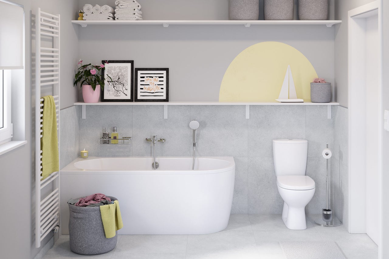 Modernes helles Badezimmer mit weißer Badewanne, Stand-WC, Handtuchheizkörper vor grauen Fliesen und zwei weißen Wandregalen mit Dekoration.