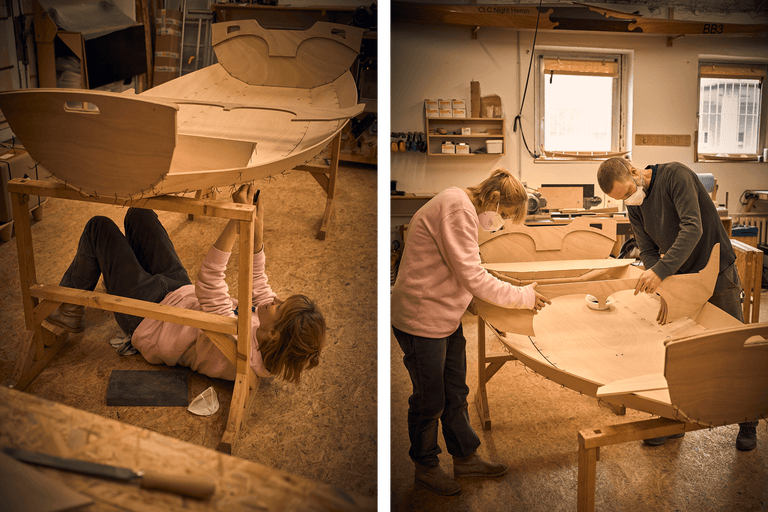 Zwei Personen bauen ein Holzboot in einer Werkstatt.