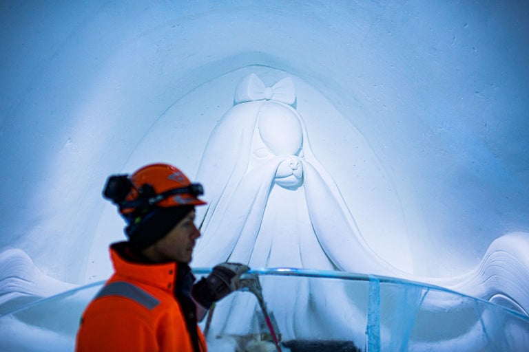 Eisstatue eines Hundes mit Schleife, gefertigt von einem Arbeiter mit Helm und Sicherheitsweste.