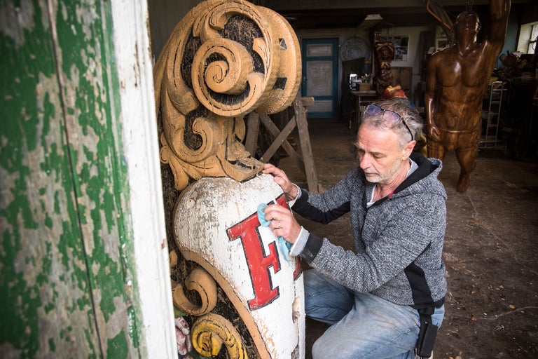 Ein Mann reinigt eine hölzerne Zierskulptur in einer Werkstatt.