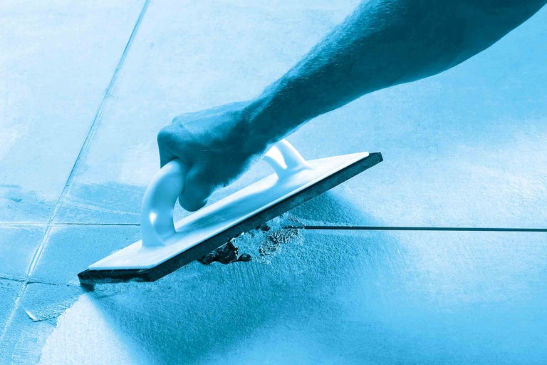 Eine Hand mit einem Fugenbrett beim Verfugen von Fliesen