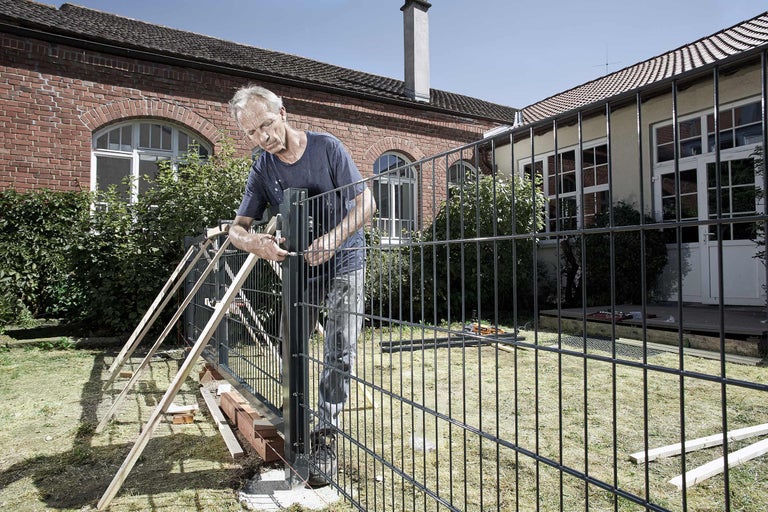 Mann montiert einen Metallzaun im Garten.