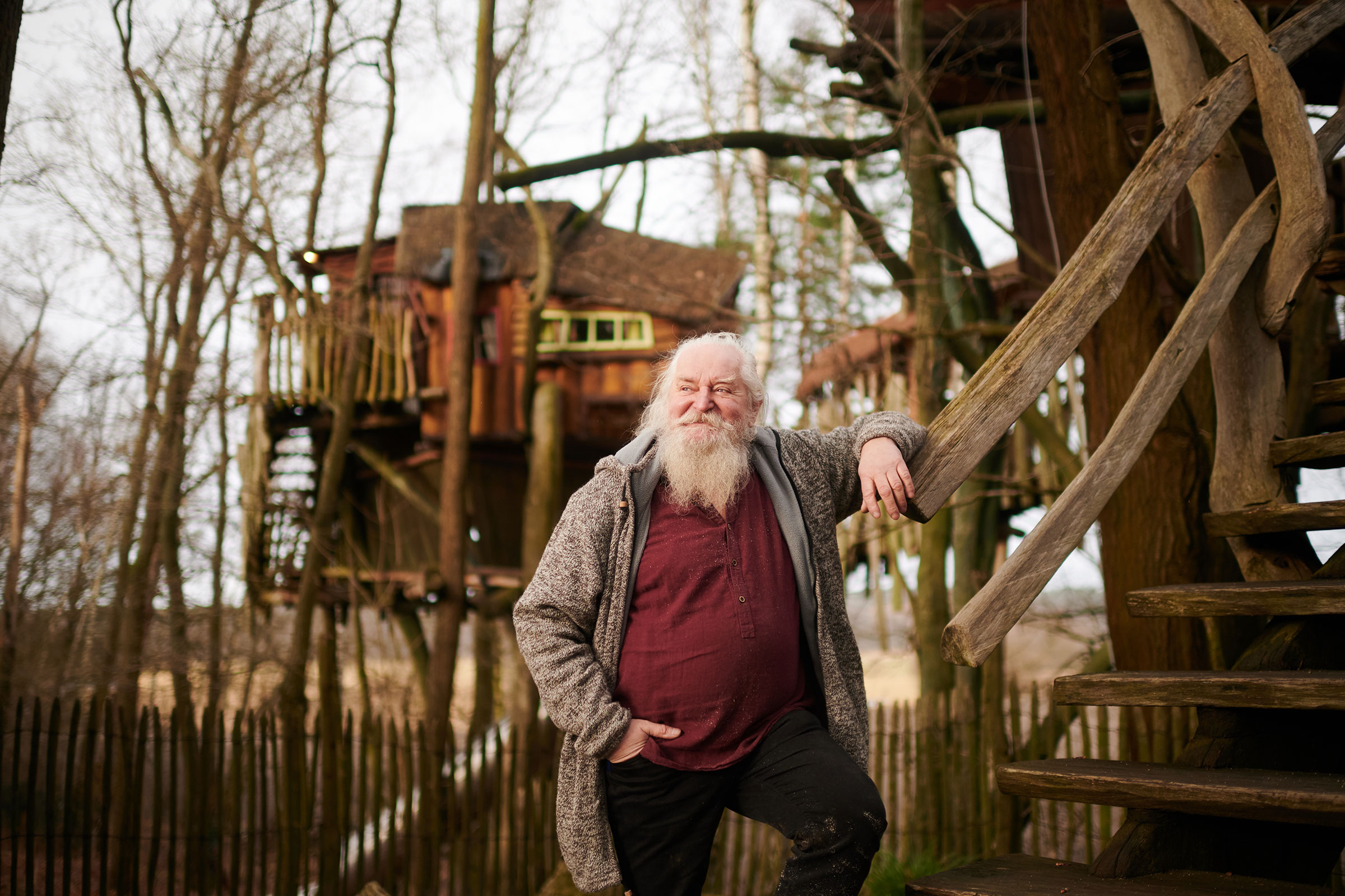 Mann steht auf einer Holztreppe vor einem Baumhaus im Wald