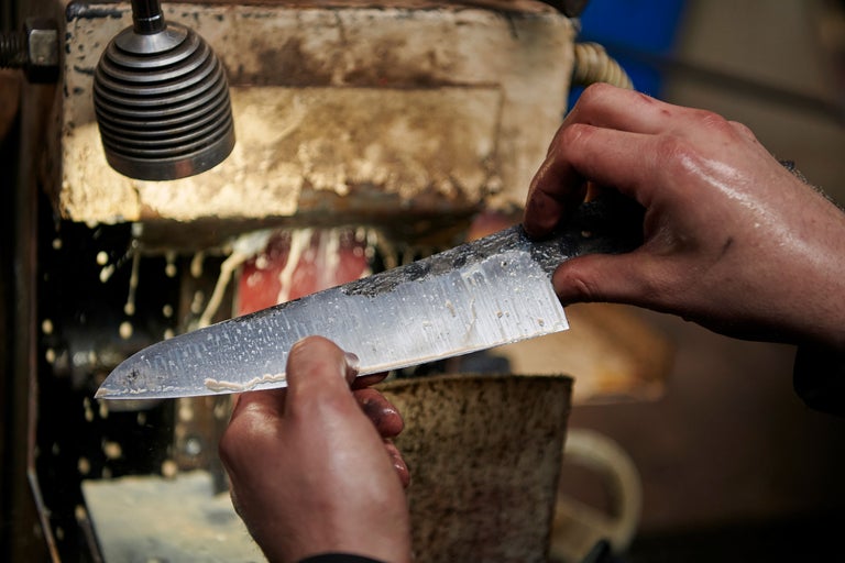 Eine Person schärft ein Messer an einer Schleifmaschine.