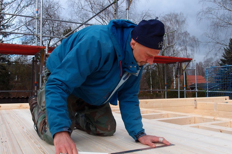 Ein Mann misst Holz auf einer Baustelle mit einem Lineal.