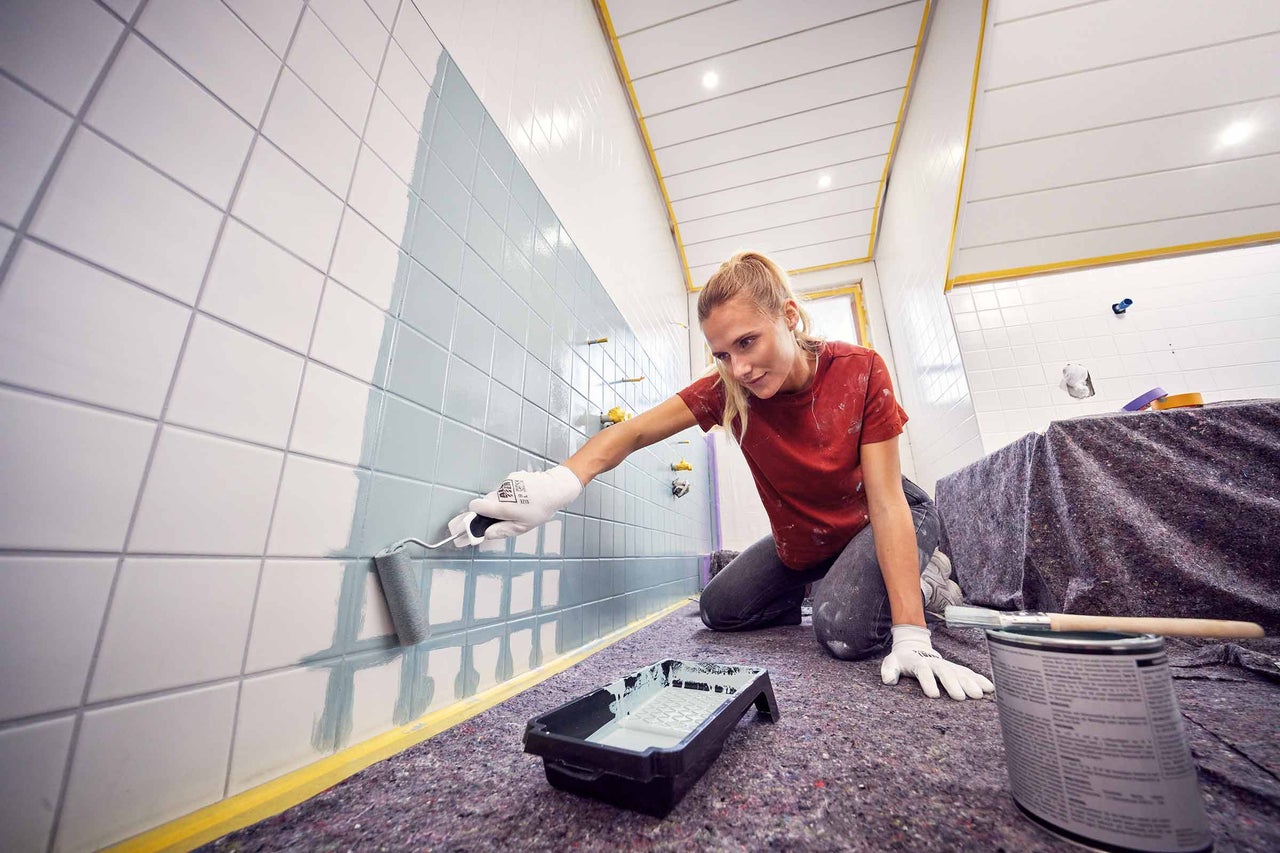 Eine Person streicht Fliesen mit einer Farbwalze.