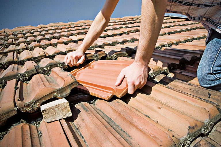 Person repariert ein Dach mit Dachziegeln