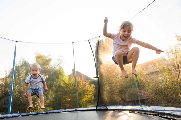 Zwei Kinder springen auf einem Gartentrampolin mit Sicherheitsnetz.