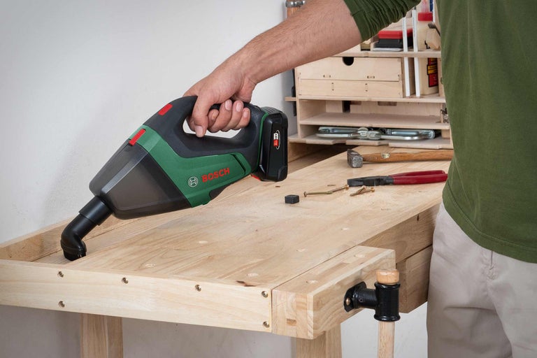 Ein Mann reinigt eine Werkbank mit einem Akku-Handsauger von Bosch