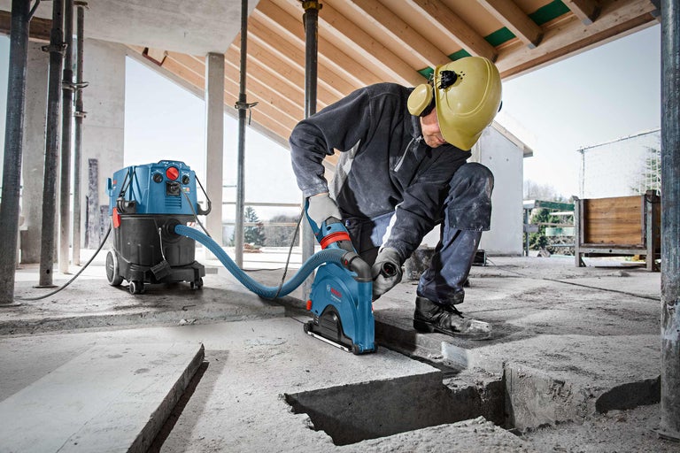 Ein Mann arbeitet mit einer Mauernutfräse und einem Industriestaubsauger auf einer Baustelle, um Schlitze in den Betonboden zu schneiden.
