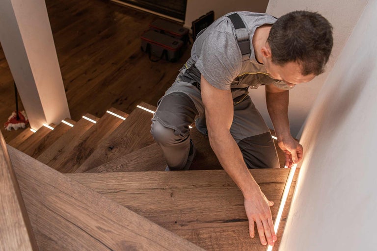 Handwerker installiert LED-Beleuchtung an Holztreppe für Hornbach