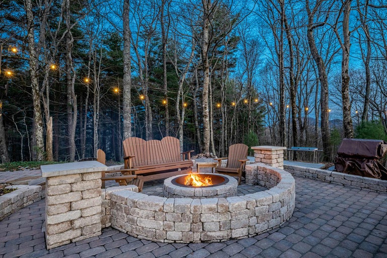 Feuerstelle umgeben von Steinmauer mit Sitzgelegenheiten im Garten bei Nacht