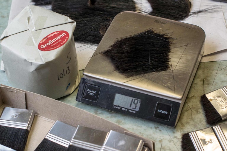 Bürstenhaare auf einer Waage, neben einer Verpackung und Pinseln