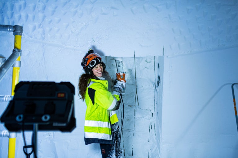 Frau mit Schutzhelm und Schutzbrille arbeitet mit einer Elektrosäge in einem Raum mit Eiswänden