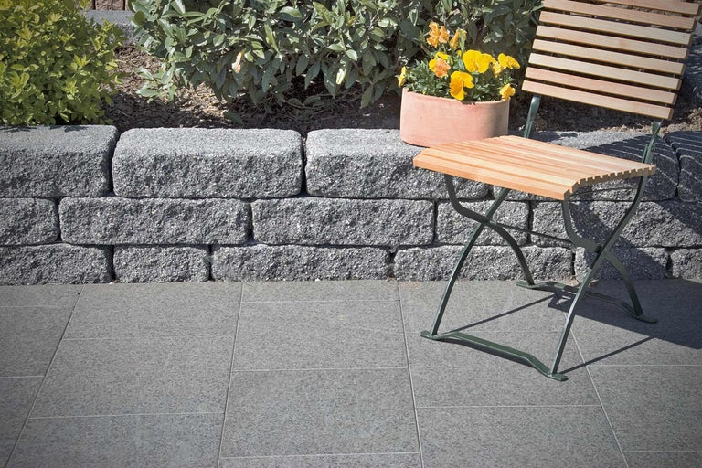 Gartenlandschaft mit Trockenmauer, Pflastersteinen, Blumen und Gartenmöbeln