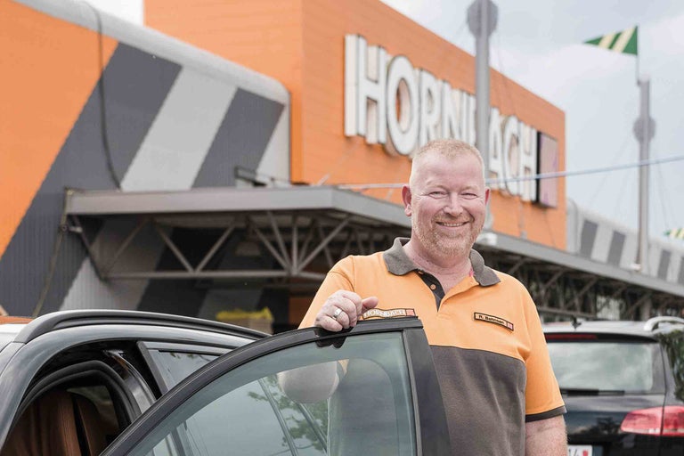 Ein Hornbach Mitarbeiter steht vor einem Auto vor dem Hornbach Baumarkt.