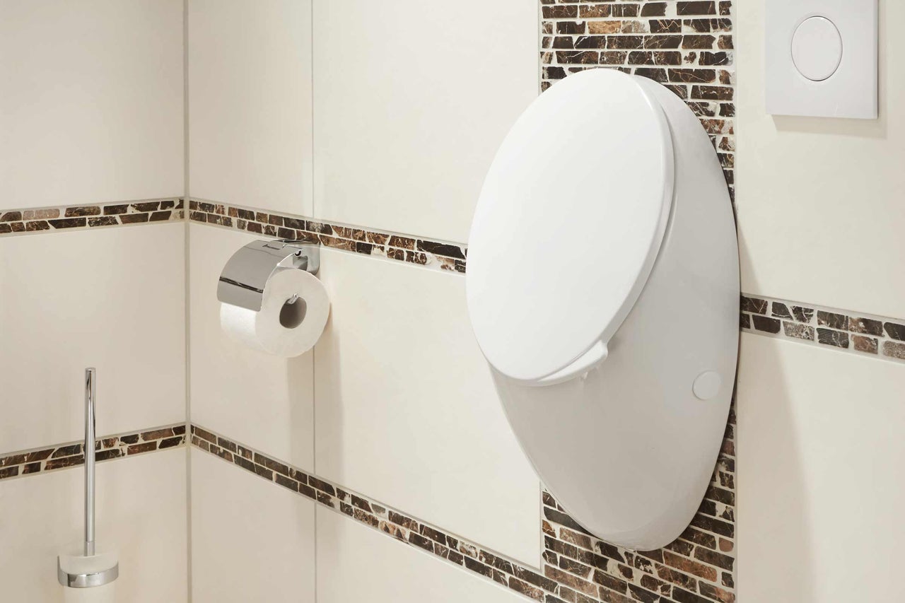 Wand-Tiefspüler-WC in einem Badezimmer mit Toilettenpapierhalter und Spülknopf