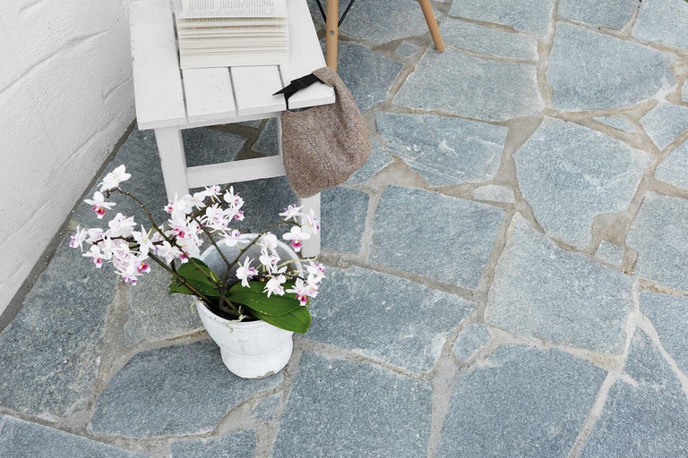 Terrasse mit Natursteinplatten, dekoriert mit Tisch, Büchern, Tasche und Topfpflanze