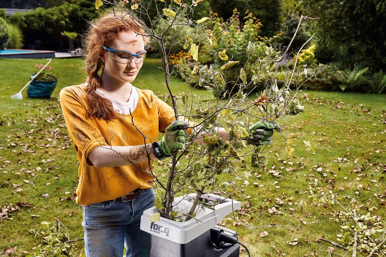 Eine Frau benutzt einen Gartenhäcksler im Garten, um Äste zu zerkleinern.
