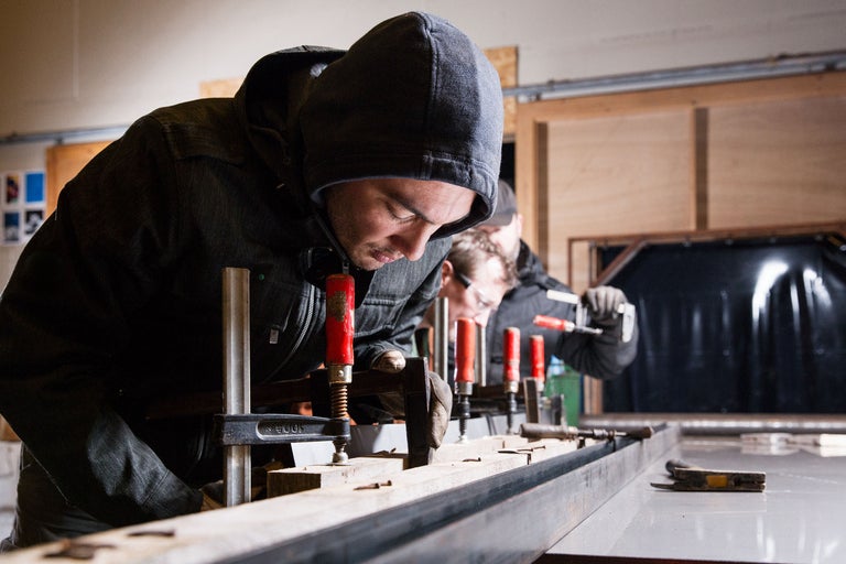 Zwei Handwerker arbeiten mit Schraubzwingen an einem Holzrahmen auf einer Werkbank.