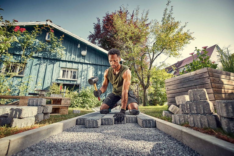 Mann verlegt Pflastersteine mit Gummihammer im Garten