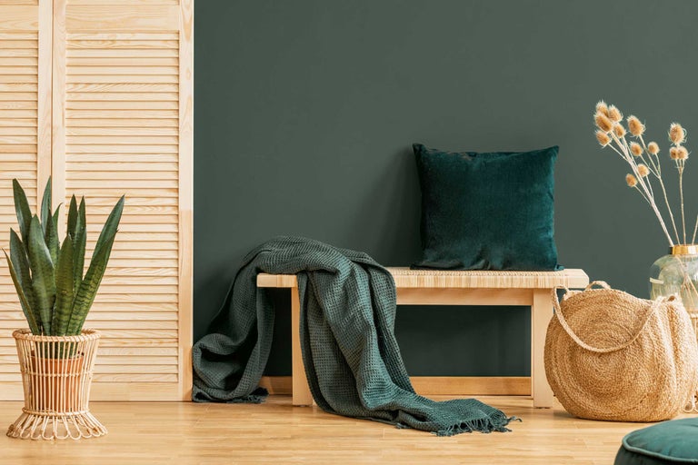 Dekoratives Wohnambiente mit Bank, Kissen, Decke, Pflanze und Flechtkorb