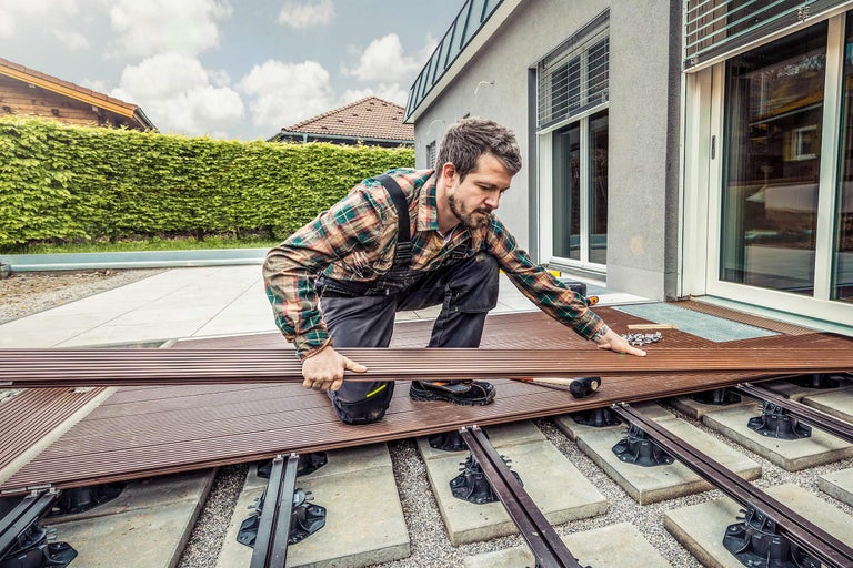 Mann verlegt Terrassendielen auf einer Terrasse mit verstellbaren Füßen.