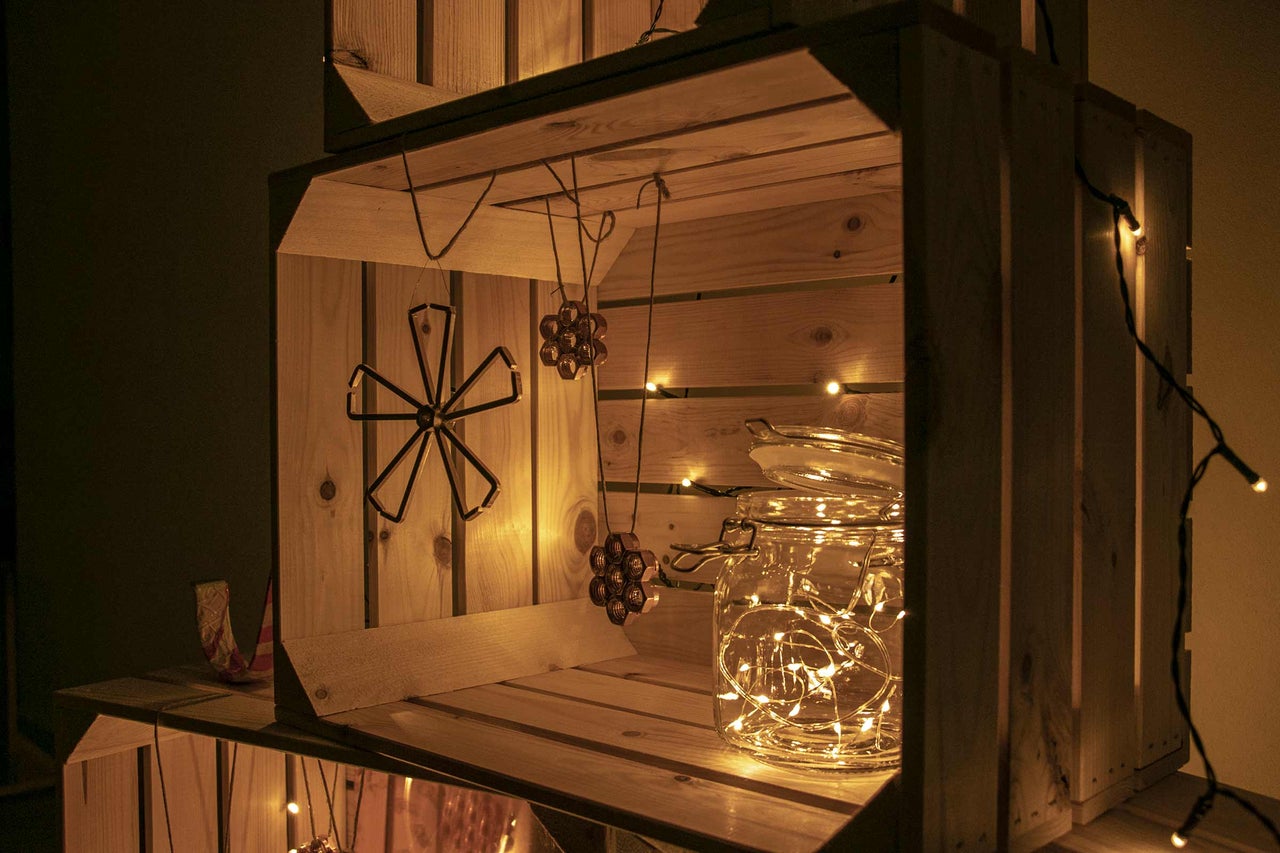 Dekoratives Arrangement mit Holzkisten, Metallanhängern, einem Einmachglas und einer Lichterkette für eine gemütliche Atmosphäre.