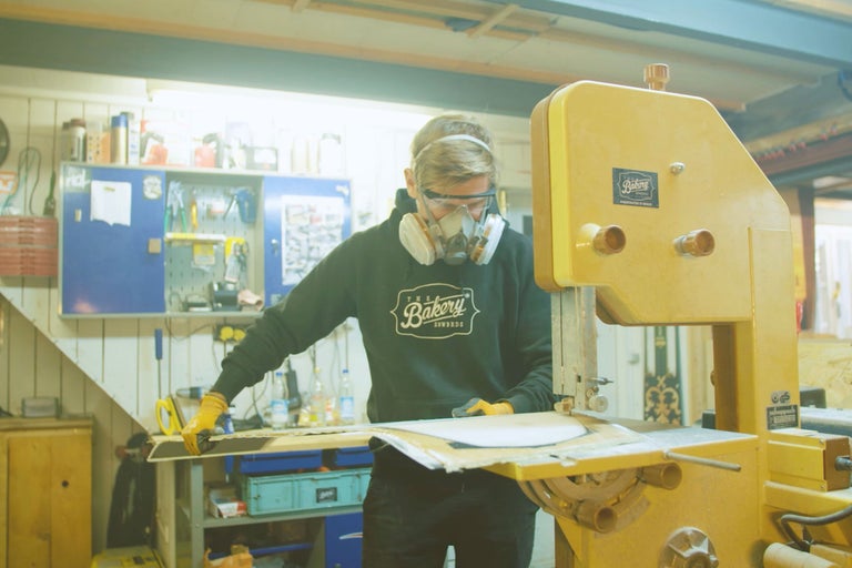 Mann mit Schutzmaske und Schutzbrille arbeitet mit einer Bandsäge in einer Werkstatt.