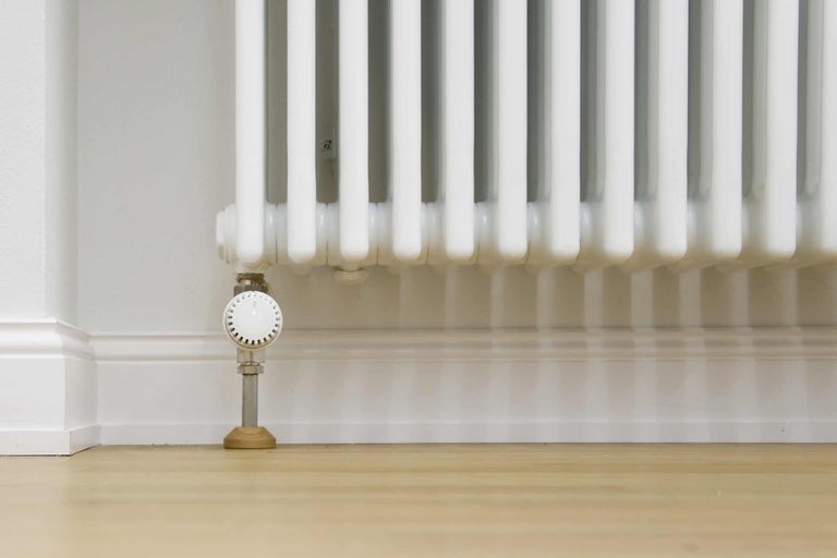 Weißer Heizkörper mit Thermostatventil an einer Wand