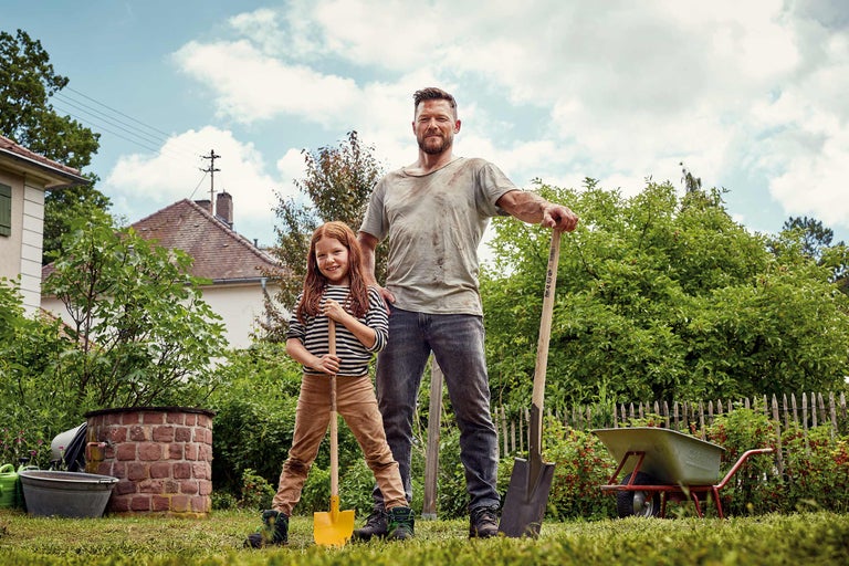 Vater und Tochter im Garten mit Spaten und Schubkarre