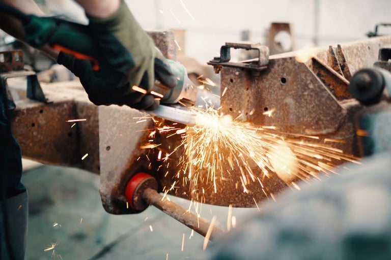 Eine Person schleift Metall mit einem Winkelschleifer, Funken sprühen.
