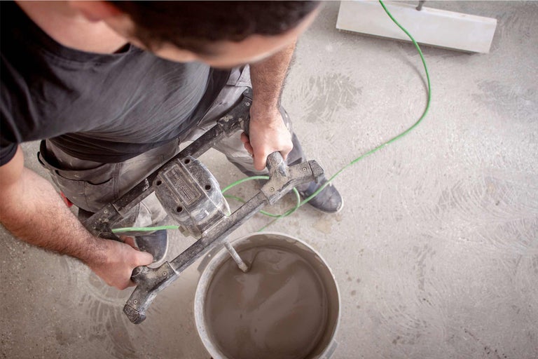 Handwerker mischt mit einem Mörtelrührer Mörtel in einem Eimer.