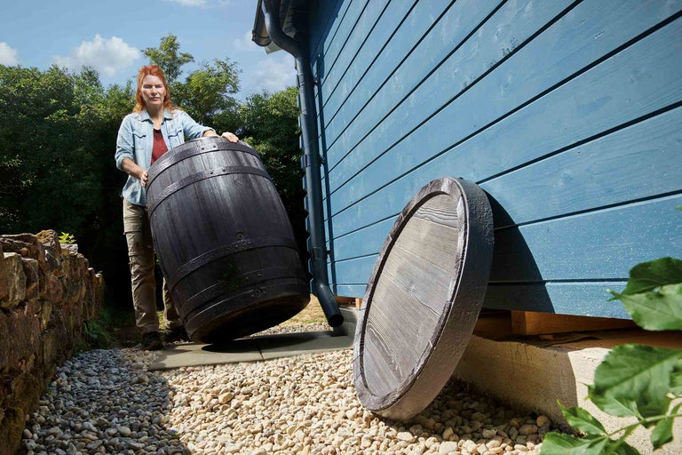 Frau transportiert Regentonne mit Deckel im Garten