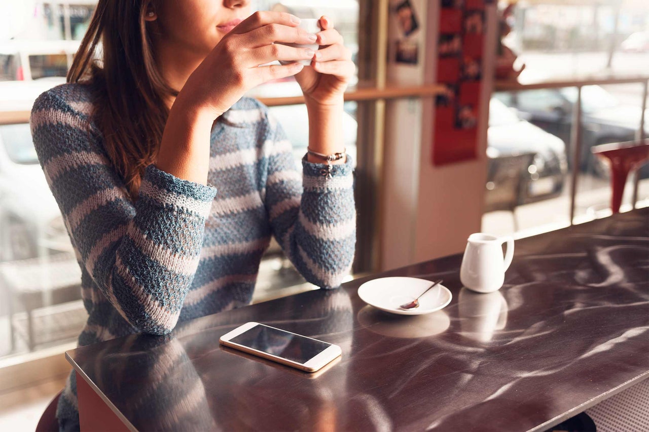 Frau trinkt Kaffee in einem Café mit Smartphone auf dem Tisch
