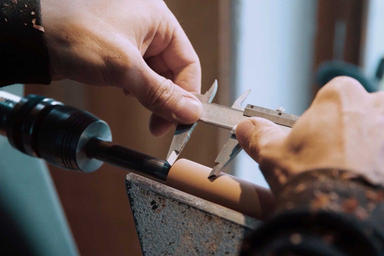 Eine Person misst ein Werkstück mit einem Messschieber auf einer Drehbank.